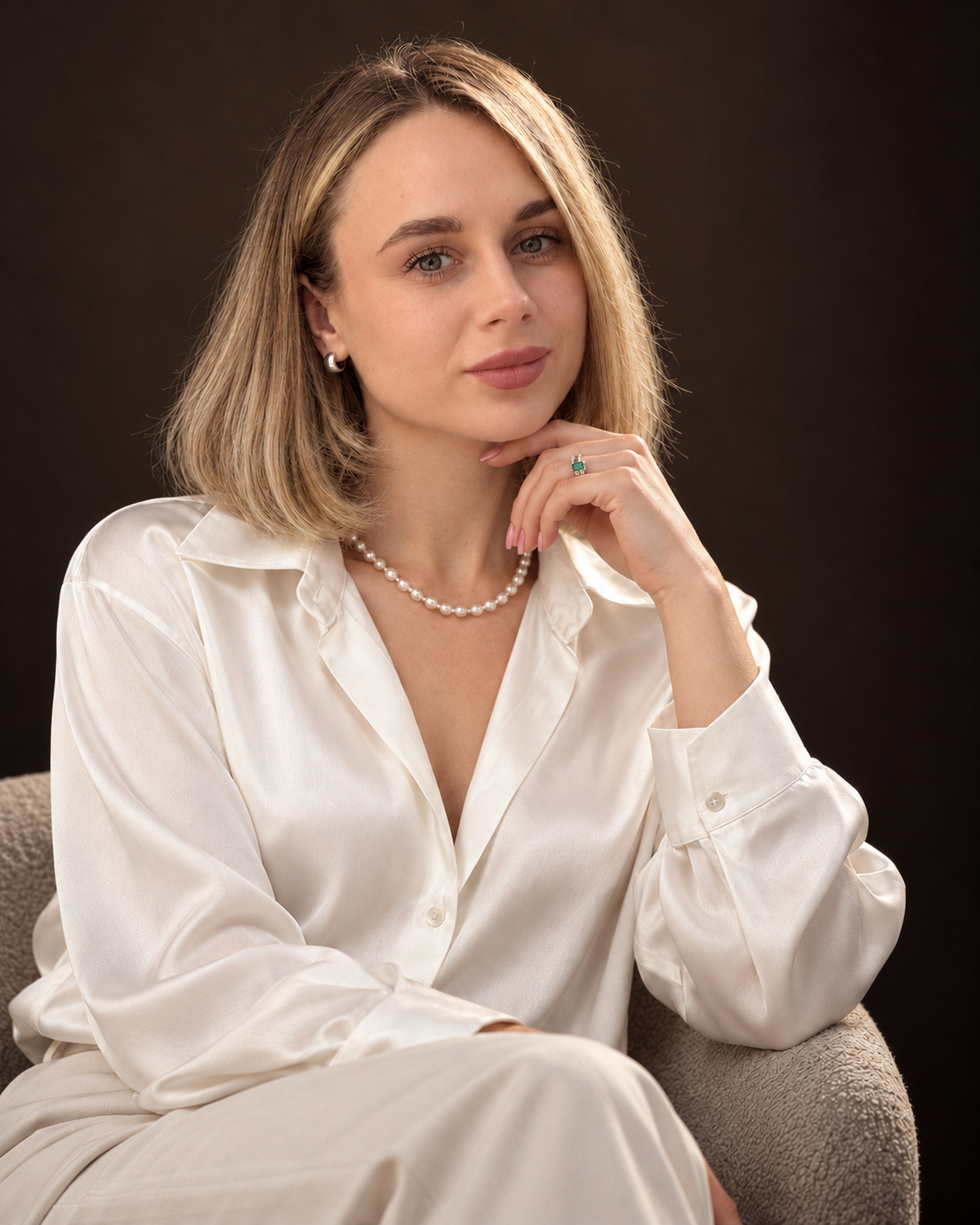 Viktoriia Quesada sentada, con camisa de seda marfil sobre fondo oscuro.